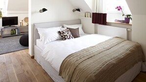 A bedroom with a bed, a television, a shelf with books and a plant, and a window with curtains. - KÖNIGSschlaf's barrier-free apartment: Chic, spacious, central! (Konstanz)