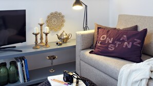 A modern living room with a grey sofa, a black ottoman, a flat-screen TV, a bookshelf, and a decorative wall piece. - KÖNIGSschlaf's barrier-free apartment: Chic, spacious, central! (Konstanz)