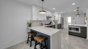 A modern kitchen with white cabinetry, a marble island, two bar stools, pendant lighting, and a built-in oven. - Peaceful Retreat Four Bedroom home in charming Shenandoah (Shenandoah)