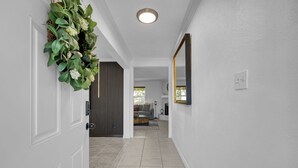 A hallway with white walls, a tiled floor, a door with a keyhole, a mirror, and a plant with white flowers. - Peaceful Retreat Four Bedroom home in charming Shenandoah (Shenandoah)