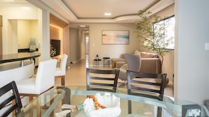 A modern living room with a glass dining table, a sofa, and a coffee table. - Apt w/ 3 BR & Grill 400m From the Beach Prs0101 (Itapema)