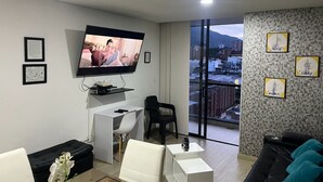 A modern living room with a flat-screen TV, a small desk, a sofa, and a balcony with city views. - Best experience: location, comfort and price (Ibagué)