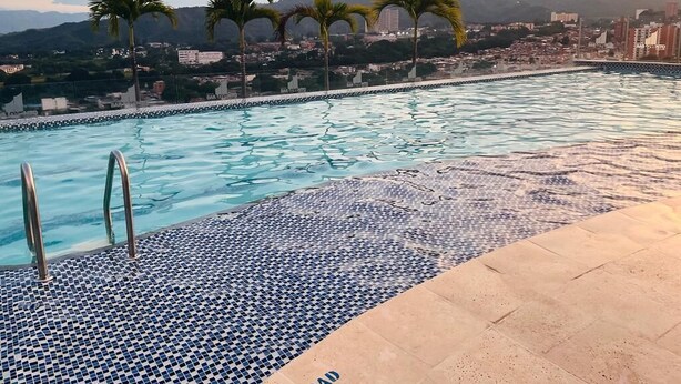 A swimming pool with a tiled edge, palm trees, and a cityscape in the background. - Best experience: location, comfort and price (Ibagué)