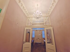 Un couloir orné d’un lustre, une porte donnant sur une pièce et une fenêtre avec des rideaux.