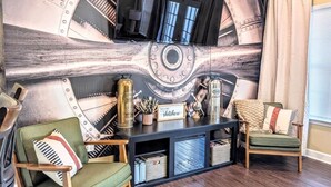 Een woonkamer met een groot muurdecor, twee groene fauteuils, een houten salontafel en een aan de muur bevestigde televisie.