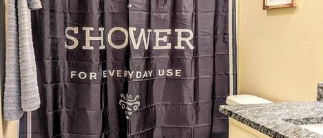 A bathroom with a black shower curtain labeled "BATHROOM SHOWER FOR EVERYDAY USE" and a framed sign that says "Wash your hands, ya filthy animal."