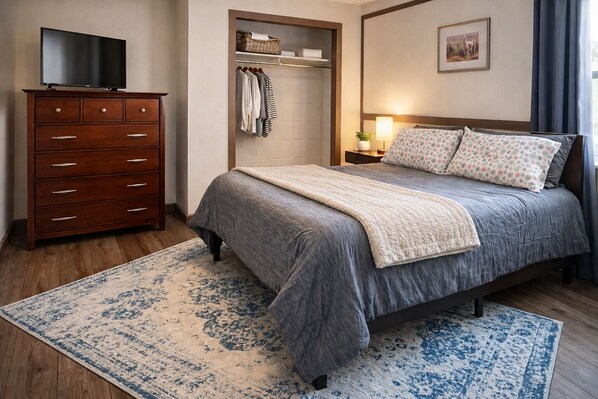 Un dormitorio con cama, cómoda, televisor, armario y ventana con cortinas.
