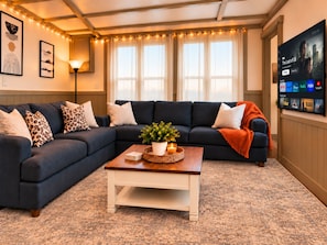 Een woonkamer met een donkerblauwe hoekbank, een witte salontafel en een grote flatscreen televisie die aan de muur is bevestigd.