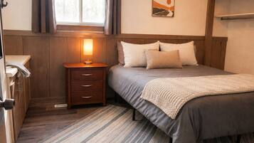 A bedroom with a bed, bedside table, lamp, and a window with curtains.