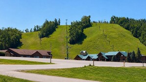 A hotel with multiple buildings, a parking lot, and a grassy hill with trees in the background.