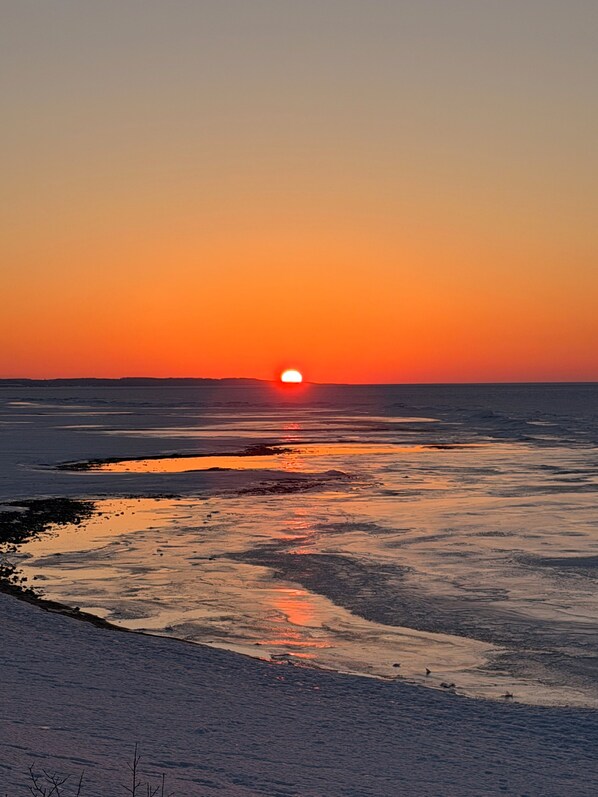 Un atardecer sobre un mar tranquilo con una costa lejana.
