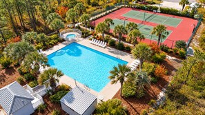 Eine Vogelperspektive zeigt einen Urlaubsort mit Schwimmbad, Tennisplätzen und einem Poolbereich mit Liegestühlen.