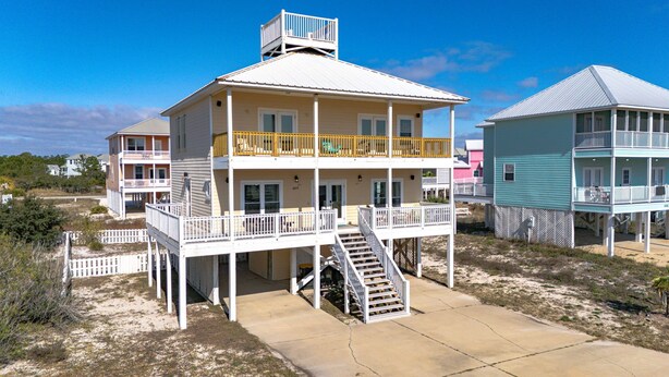Una casa affacciata sulla spiaggia con più piani, balconi, un portico coperto e una scalinata che conduce ai livelli superiori.