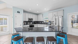 Una cucina moderna con mobili bianchi, una grande isola con sgabelli, elettrodomestici in acciaio inossidabile e vista all'esterno.