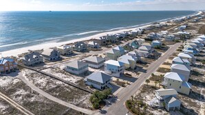 Vista aerea di una zona residenziale costiera con case lungo la spiaggia, una strada e un molo.