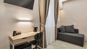 A modern hotel room with a desk, chair, and a sofa.