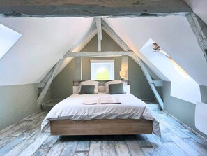 Un dormitorio con techo inclinado, una cama con almohadas, una mesita de noche y una ventana con vistas.