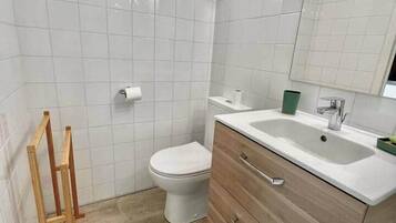 Een badkamer met witte tegels, een toilet, een houten wastafelmeubel met lades en een spiegel.