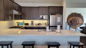 Uma cozinha moderna com armários de madeira escura, uma geladeira de aço inoxidável, micro-ondas e uma ilha grande com banquetas.