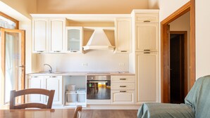 A compact kitchen with white cabinetry, a built-in oven, and a dining area with a wooden table and chairs.