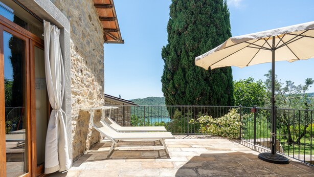 A stone patio with a lounge chair and umbrella, a tall tree, and a view of the landscape.