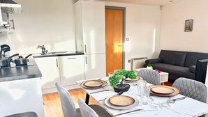 Une cuisine moderne avec des meubles blancs, un plan de travail noir et un coin repas doté d’une table en marbre, mise pour quatre personnes.
