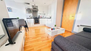 Un salon moderne avec un canapé gris, une table basse blanche et un téléviseur à écran plat.
