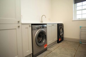 A laundry room with two front-loading washing machines, a sink, and a window. - Gelli Genlas, Llanarth (New Quay)