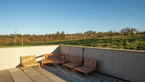 Terraza en la azotea con tres bancos de madera y vistas a un campo verde y árboles.