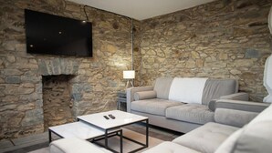 Una habitación con paredes de piedra, un televisor de pantalla plana, un sofá, una mesa de centro y una lámpara.