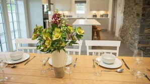 Una mesa de comedor dispuesta con platos, fuentes y cubiertos blancos, y un florero con flores en el centro.
