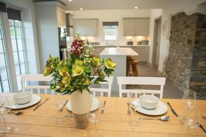 A dining table set with white plates, bowls, and cutlery, with a vase of flowers in the center. - Gelli Genlas, Llanarth (New Quay)