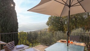 A balcony with a table, chairs, an umbrella, and a view of a forested landscape. - Green Deluxe Casa De Fiori – Agriturismo with Experiences, Breakfast Included - Le Ceregne Bio (Pieve Santo Stefano)