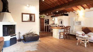 A cozy living area with a fireplace, stone fireplace surround, wooden ceiling beams, and a dining area with a stone island. - Green Deluxe Casa De Fiori – Agriturismo with Experiences, Breakfast Included - Le Ceregne Bio (Pieve Santo Stefano)