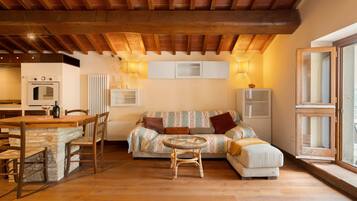 A cozy living area with a wooden ceiling, a sofa, a dining table with chairs, and a small round table with a chair.