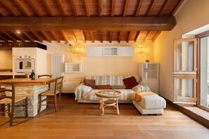 A cozy living area with a wooden ceiling, a sofa, a dining table with chairs, and a small round table with a chair. - Green Deluxe Casa De Fiori – Agriturismo with Experiences, Breakfast Included - Le Ceregne Bio (Pieve Santo Stefano)