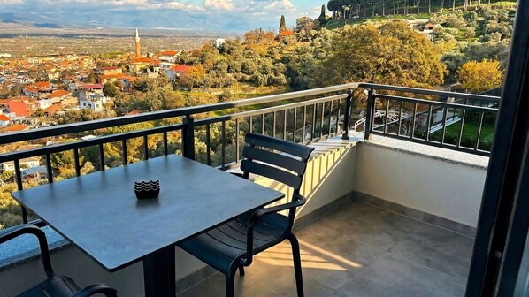A balcony with a table and chairs, overlooking a town with buildings and trees. - TopTepeHome (Tire)