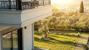 Un bâtiment moderne doté d’un balcon donnant sur un jardin aménagé et offrant une vue lointaine sur la ville.
