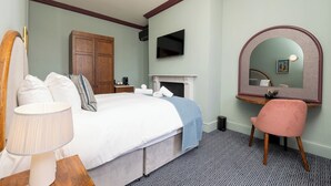 Een slaapkamer met een bed, een bureau, een stoel, een televisie, een open haard en een spiegel.