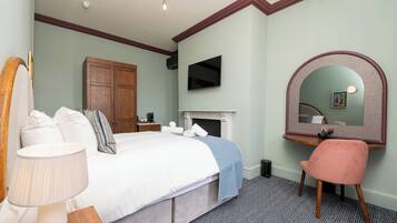 A bedroom with a bed, a desk, a chair, a TV, a fireplace, and a mirror.