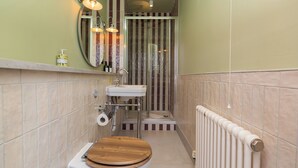 Een kleine badkamer met een houten toilet, een witte wastafel, een spiegel en een douche met gestreepte tegels.