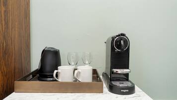 A coffee machine with two white mugs and two empty glasses on a tray.