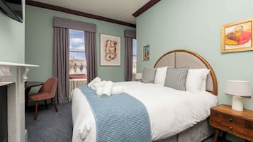 A hotel room with a large bed, a desk, a chair, and artwork on the walls.