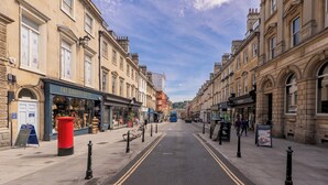 Une rue bordée de boutiques des deux côtés, dont une devanture bien visible avec une enseigne indiquant « FAT GIRAFFE GIFTS ».