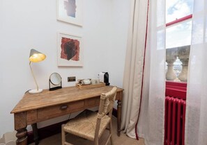 Un bureau en bois, une lampe, une chaise, un radiateur et une fenêtre avec des rideaux.