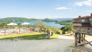 A view of a lake with a wooden bridge, a stone building, and a pool area with umbrellas. - Il Bacio – Agriturismo with Experiences, Breakfast Included - Le Ceregne Bio (Pieve Santo Stefano)