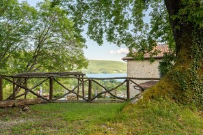 Un ponte di legno rustico, un edificio in pietra e un lago con colline sullo sfondo.