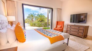 Een hotelkamer met een groot bed, een televisie, een stoel en uitzicht op palmbomen.