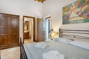 Une chambre à coucher avec un lit, une armoire en bois, une salle de bain avec un lavabo et un tableau accroché au mur.