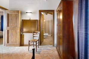 Une pièce avec une chaise en bois, un meuble en bois et une salle de bain visible à travers une porte ouverte.
